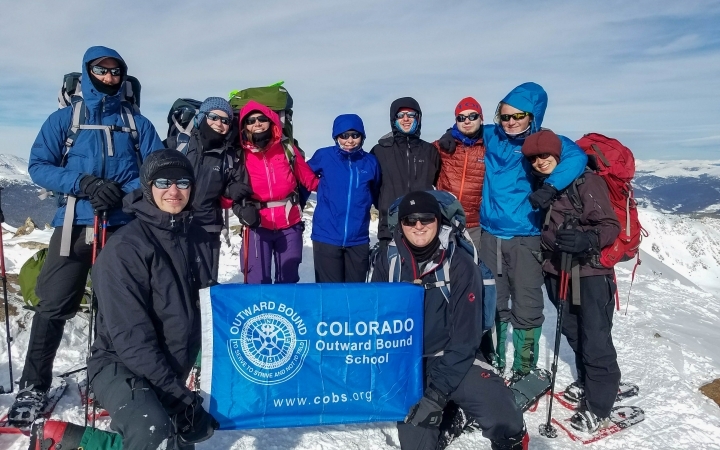 a group of people stand atop a snowy summit with an outward bound flag